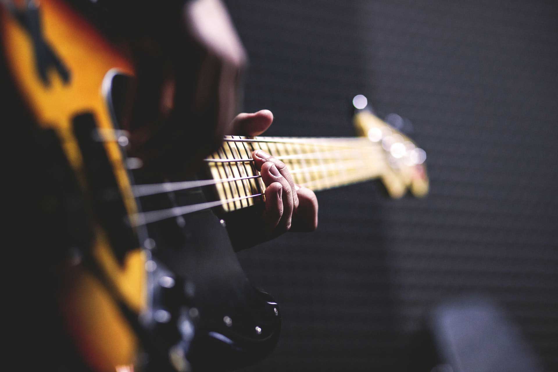 person-playing-sun-burst-electric-bass-guitar-in-bokeh-96380